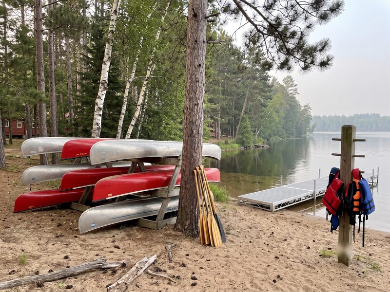 Wenonah canoes stacked on the shoreline rack, paddles leaning alongside