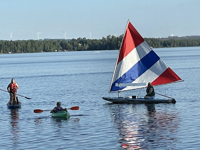 A kayak, a paddleboard, and a sailing dinghy rafted up together on open water