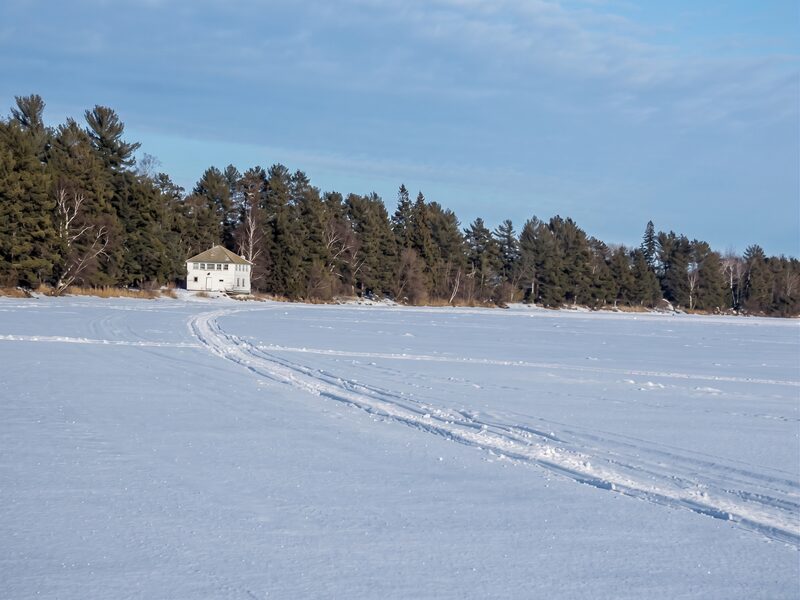 The frozen lake in deep winter, snow drifted against the treeline