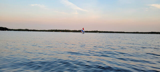 A lone sailboat crossing wide pastel water at dusk
