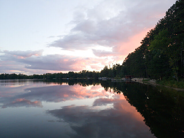Pink sunset clouds mirrored on still water along the boathouse shoreline