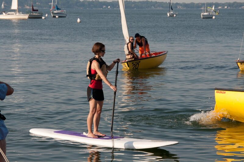 A paddleboarder gliding through golden evening light, sailboats scattered behind